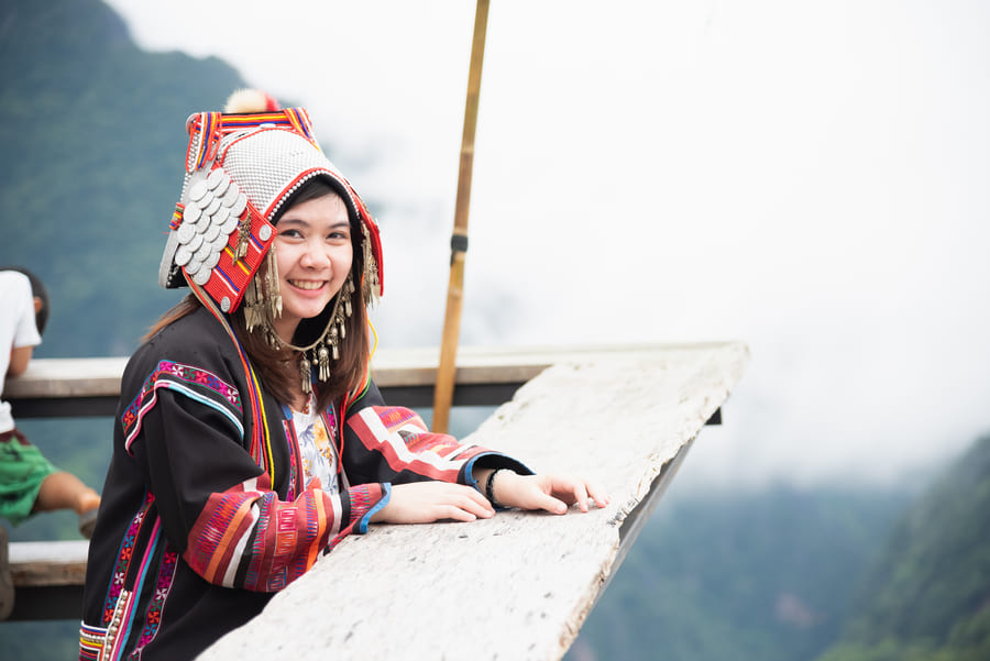 Mujer sonriente con traje tradicional étnico y tocado ornamental en mirador con montañas neblinosas al fondo